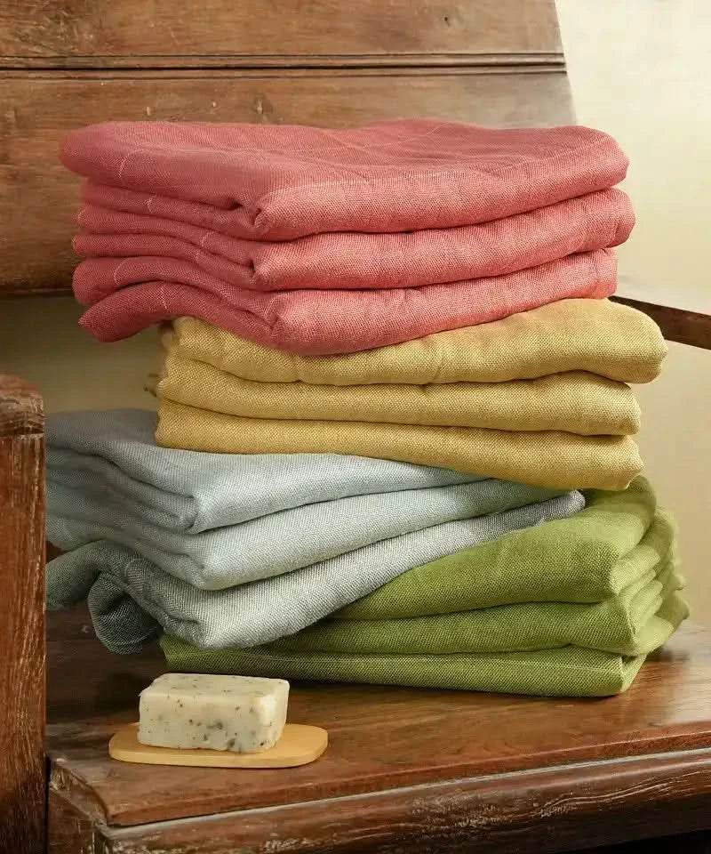 Stack of folded towels in Apricot Brandy ( Red), yellow , green, and gray on a wooden surface with a bar of soap.