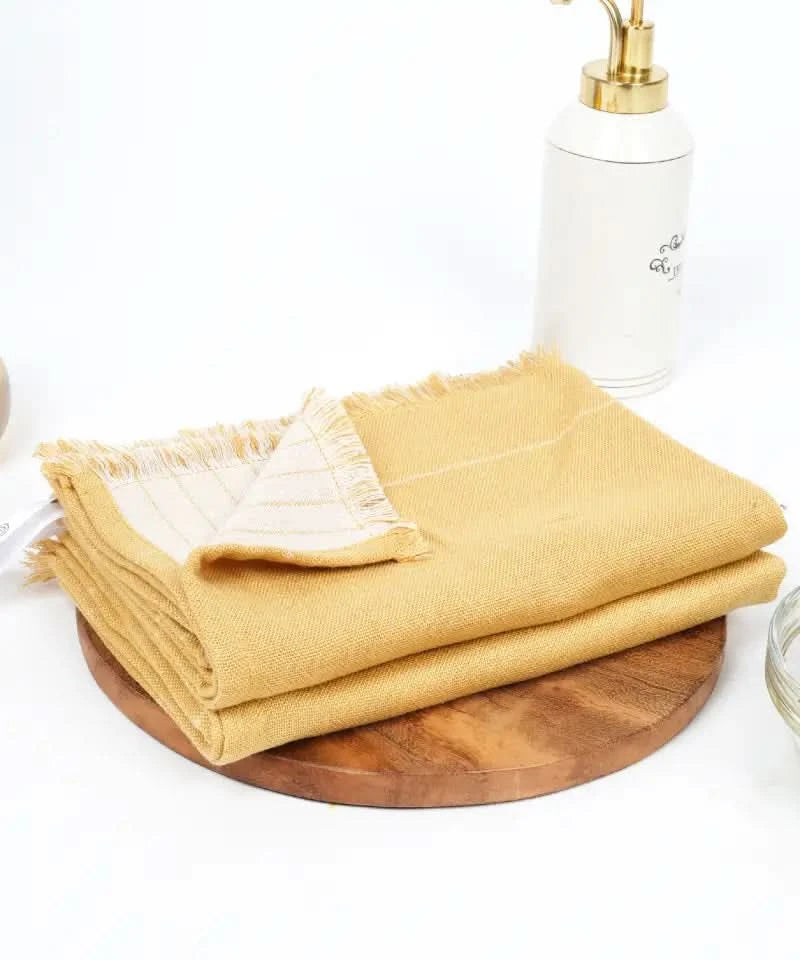 Mustard yellow towels on a wooden tray with a white bottle and glass container in the background.