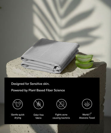 Gray towel on a stone surface with aloe vera leaves, labeled as sensitive skin product.