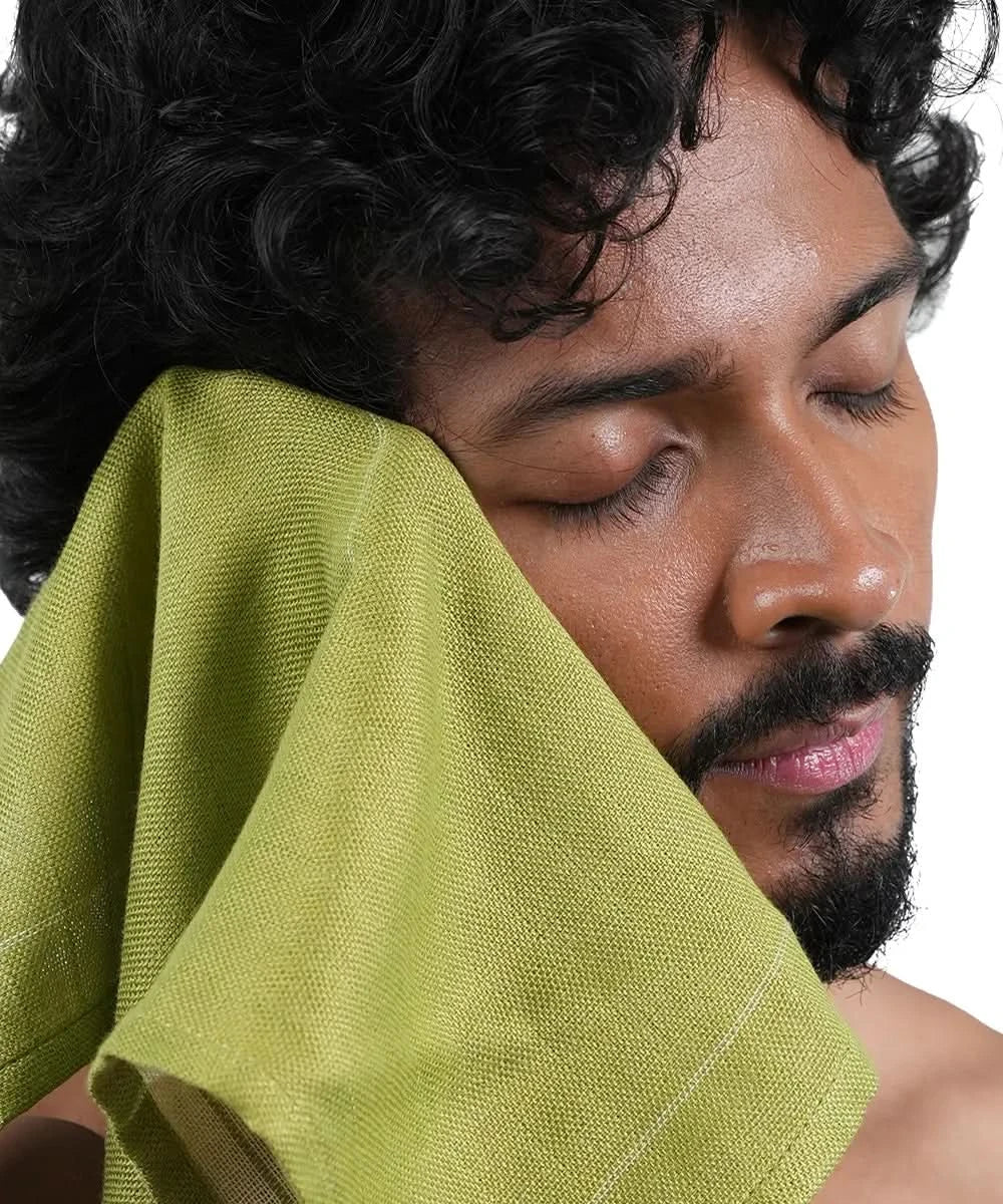 Man with a green towel on his face against a white background