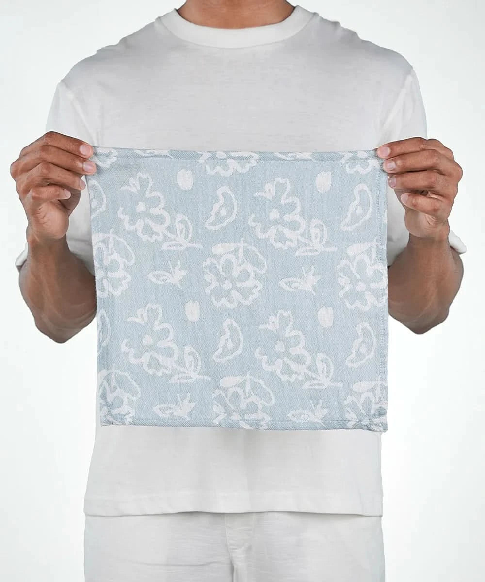 Person holding a light blue fabric with white floral patterns against a white background