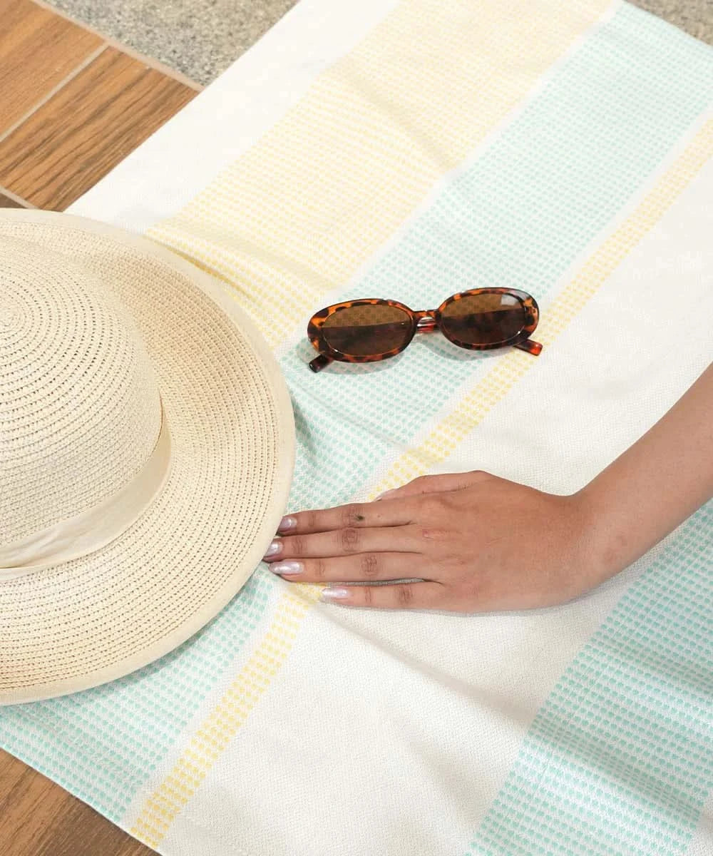 Beige sun hat and tortoise shell sunglasses on a bamboo dobby with a hand reaching out.