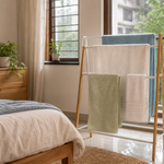 Freestanding bedroom towel stand with well-spaced towels drying near a bright Indian window
