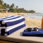Folded striped beach towels with a smaller separate face towel, sunscreen, and sunglasses beside the sea