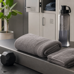 A gym bench with a workout towel, a separate smaller face towel, and a water bottle in a clean locker-room setting
