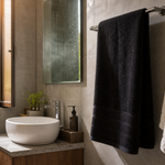 Folded black towel on a bathroom rail beside a lighter separate face towel in a humid Indian bathroom