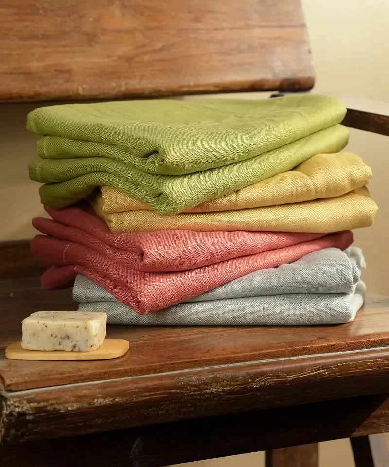 Stack of folded auvera double cloth bath towel on a wooden surface with a bar of soap.