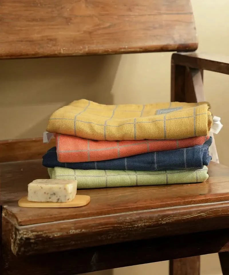 Stack of folded Banana Double cloth bath towel - 4 pieces on a wooden surface with a wooden chair in the background.
