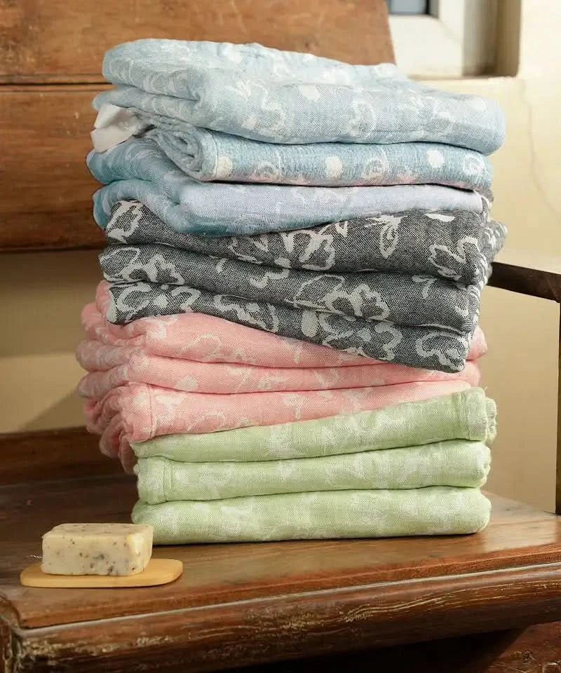 Stack of folded Banana jacquard floral towels in various colors on a wooden surface.
