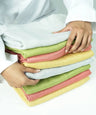 Stack of folded aluvera double cloth bath towels held by a person on a white background