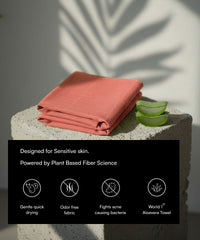 Folded red (Apricot Brandy) towel on a stone surface with aloe vera slices, set against a neutral background.