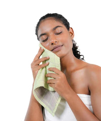 Woman using a green towel on her face against a white background