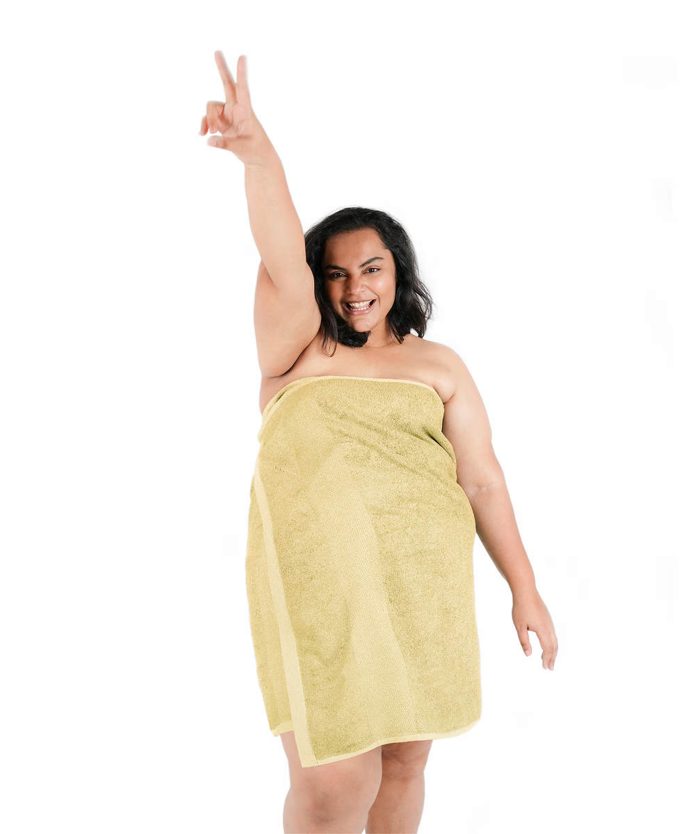 Woman wrapped in a yellow towel, making a peace sign on a white background