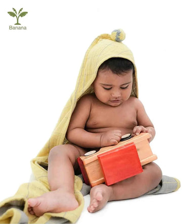 Baby playing with a wooden toy wrapped in a yellow towel on a white background
