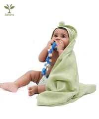 Baby wrapped in a green towel holding a blue and wooden toy on a white background