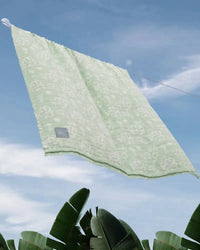Green towel hanging on a clothesline against a blue sky with clouds