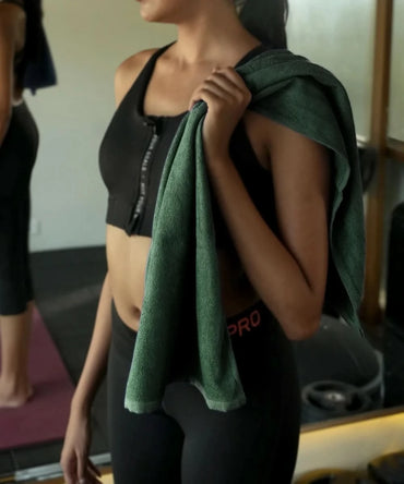 Person in black athletic wear holding a banana terry gym towel in a gym setting