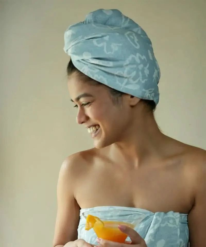 Woman with a blue patterned towel on her head holding an orange against a plain background