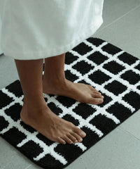 Person wearing a white bathrobe standing on a black and white checkered bath mat.