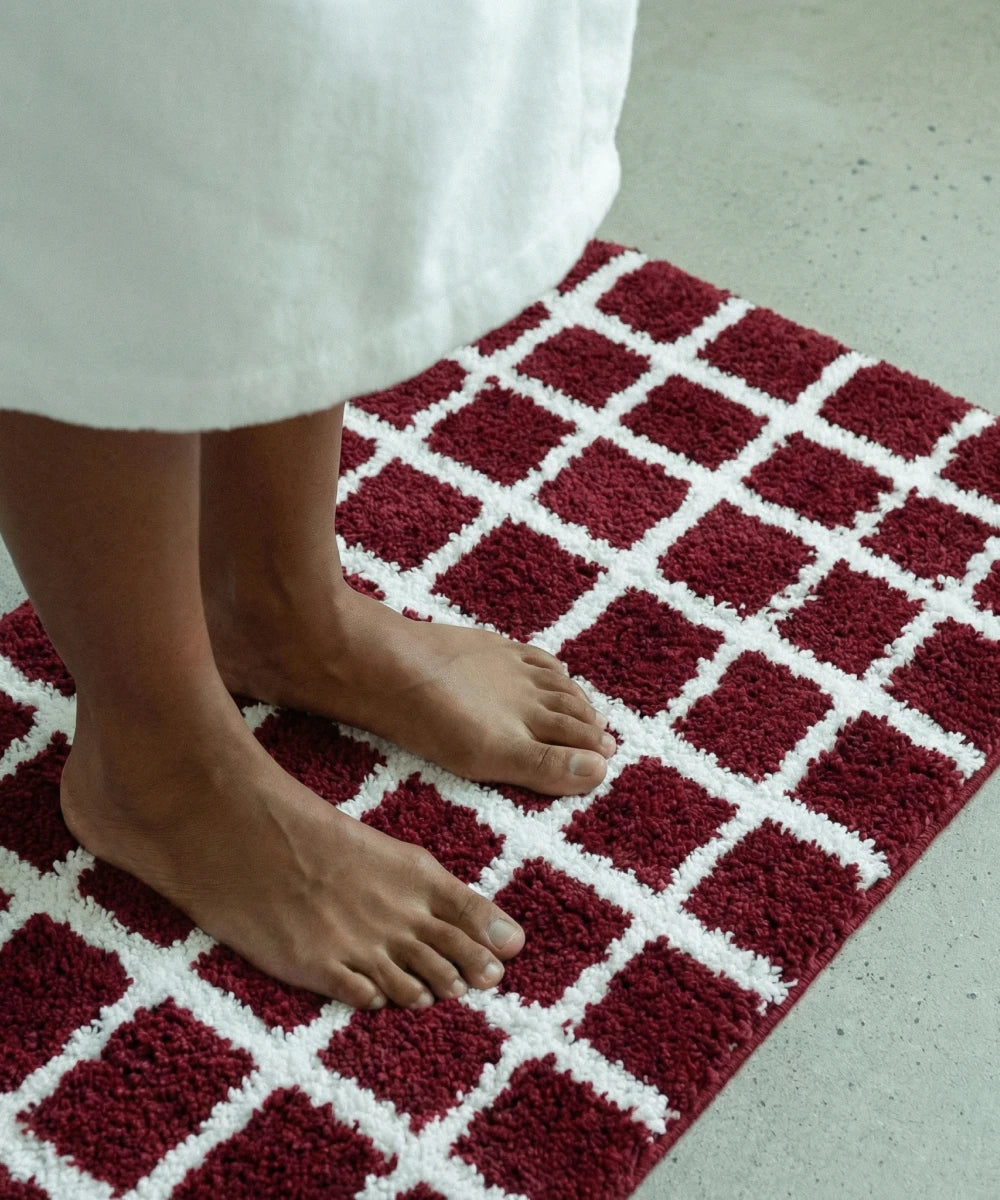 Red and white checkered bath mat with a person's feet stepping onto it.
