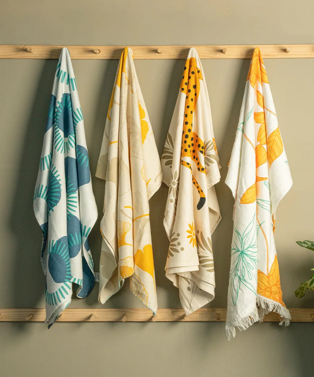 Four patterned thirsty towels hanging on a wooden rack against a beige wall.