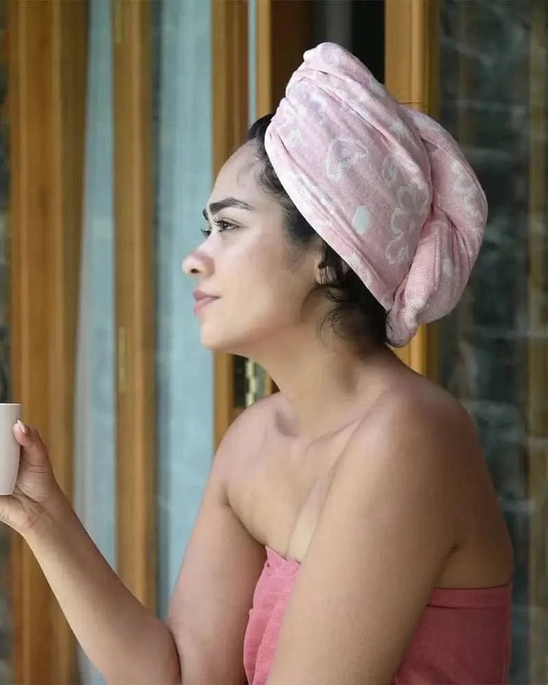 Woman with a Banana jacquard floral towel  - coral color wrapped around her head, holding a cup, in front of a window.