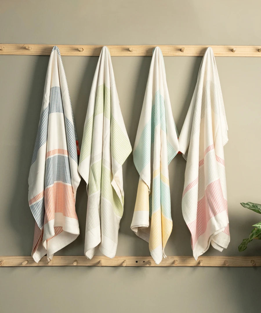 Four bamboo dobby towels hanging on a wooden rack against a beige wall.