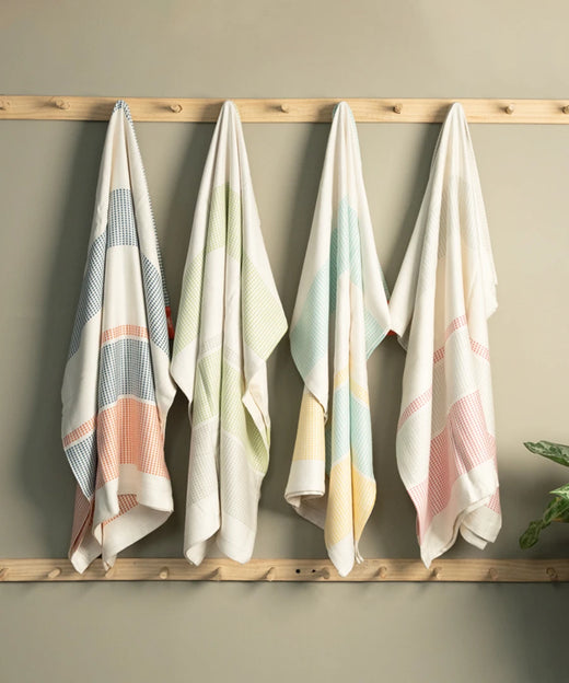 Four bamboo dobby towels hanging on a wooden rack against a beige wall.