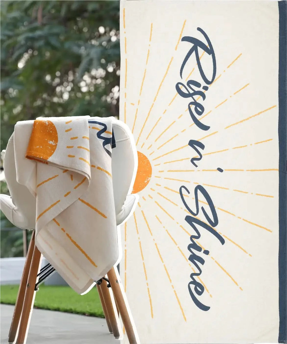 Towel with 'Rise & Shine' text draped over a chair outdoors