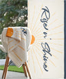 Towel with 'Rise & Shine' text draped over a chair outdoors