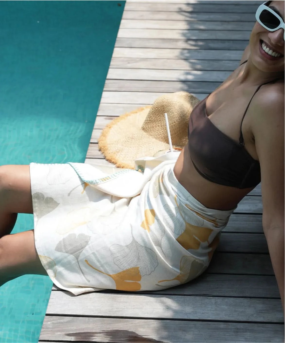 Person sitting by a pool with a gingko garden towel and sunglasses