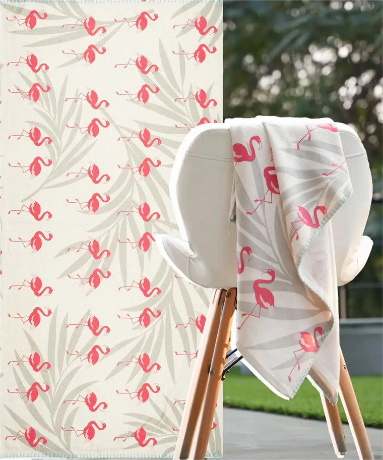 Floral-patterned towel with pink flamingo design draped over a chair outdoors.