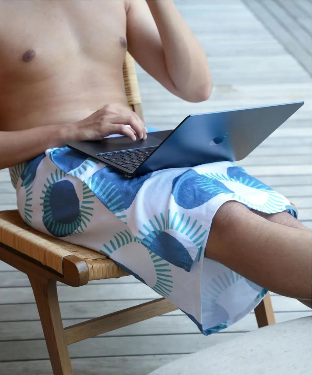 Person sitting on a chair using a laptop, wearing patterned shorts.