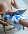 Person sitting on a chair using a laptop, wearing patterned shorts.