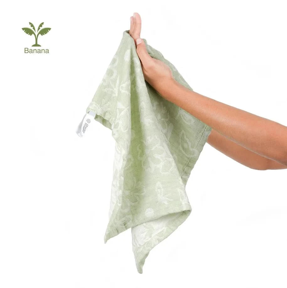 Hand holding a pastel green banana jacquard floral towel with a logo in the corner
