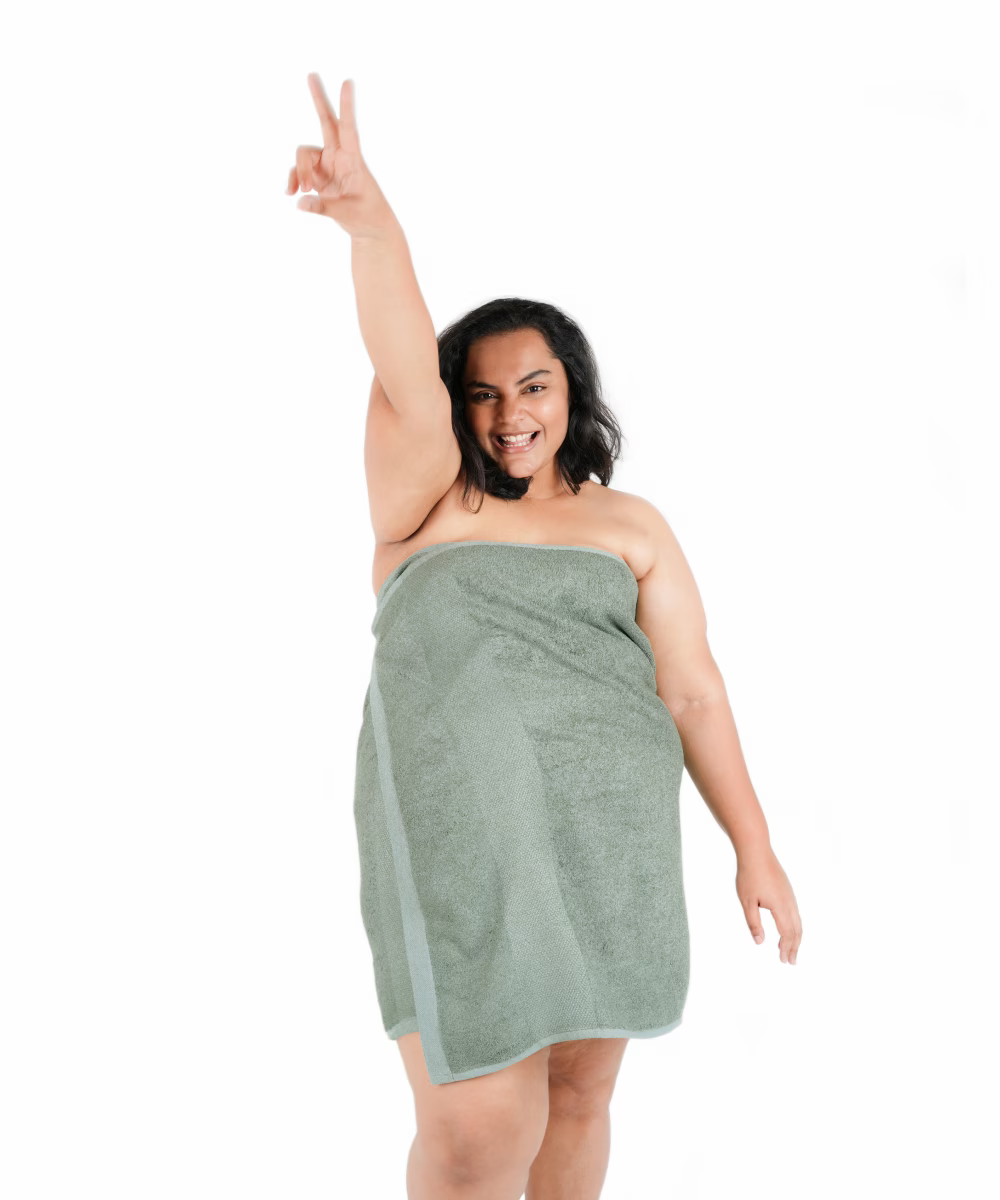 Woman wrapped in a sage green towel, making a peace sign on a white background