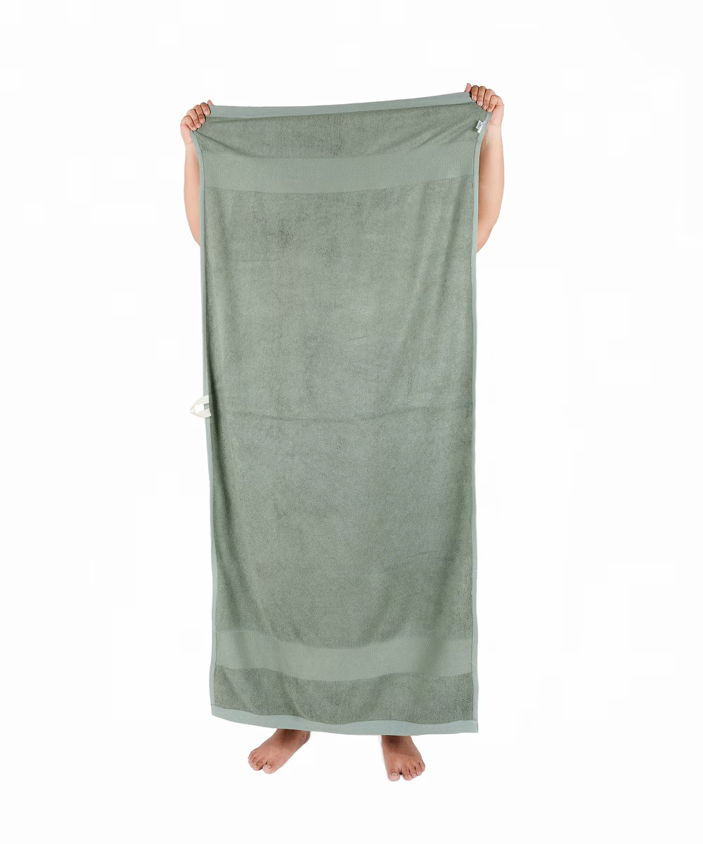 Person holding a sage green towel on a white background