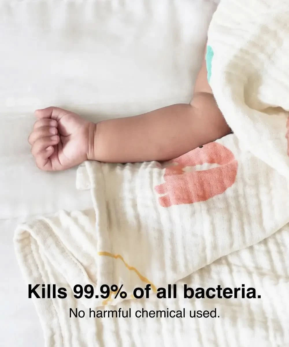 Baby arm wrapped in a soft bamboo swaddle with text about bacteria-killing properties.