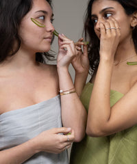 Two women applying strips to their faces, one in a gray towel and the other in a green towel.