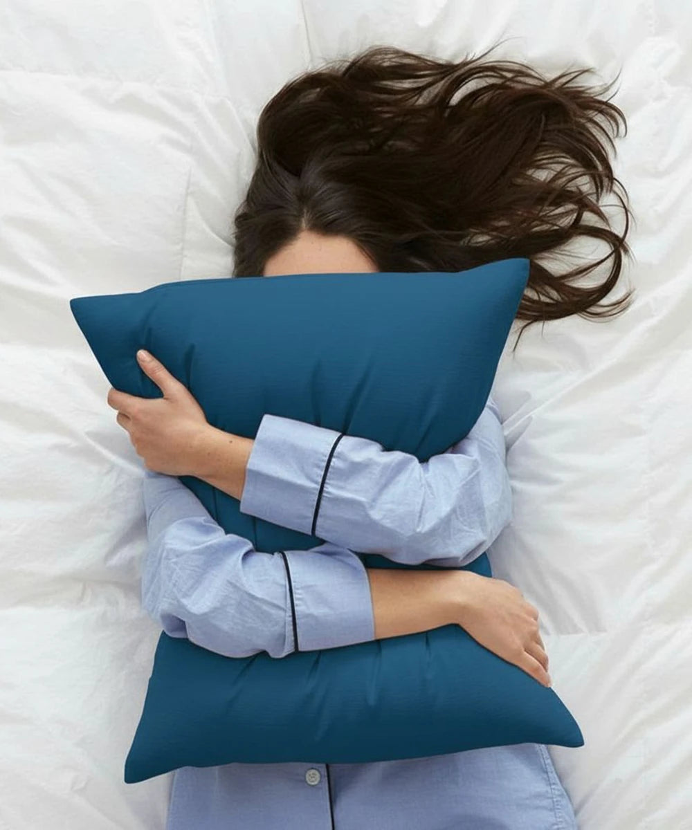 Person lying on a bed with a blue pillow, wearing light blue pajamas.