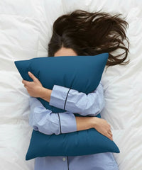 Person lying on a bed with a blue pillow, wearing light blue pajamas.