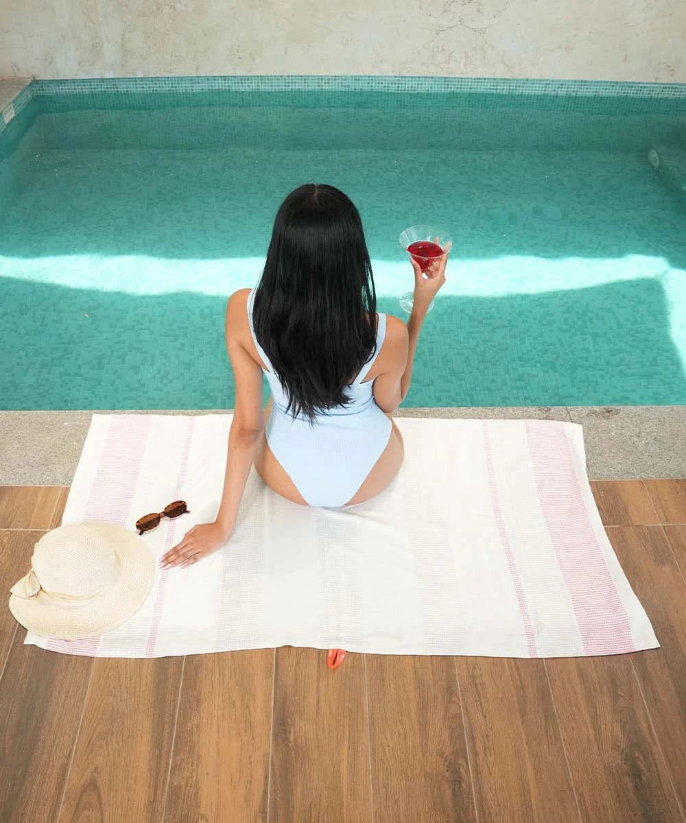 Woman sitting by a pool holding a glass of red wine on a towel.