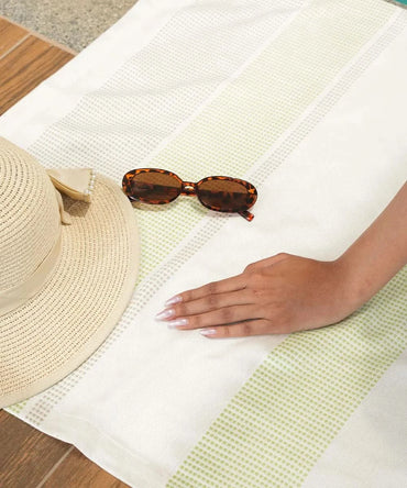 Sunglasses and a straw hat on a white towel with a hand reaching out