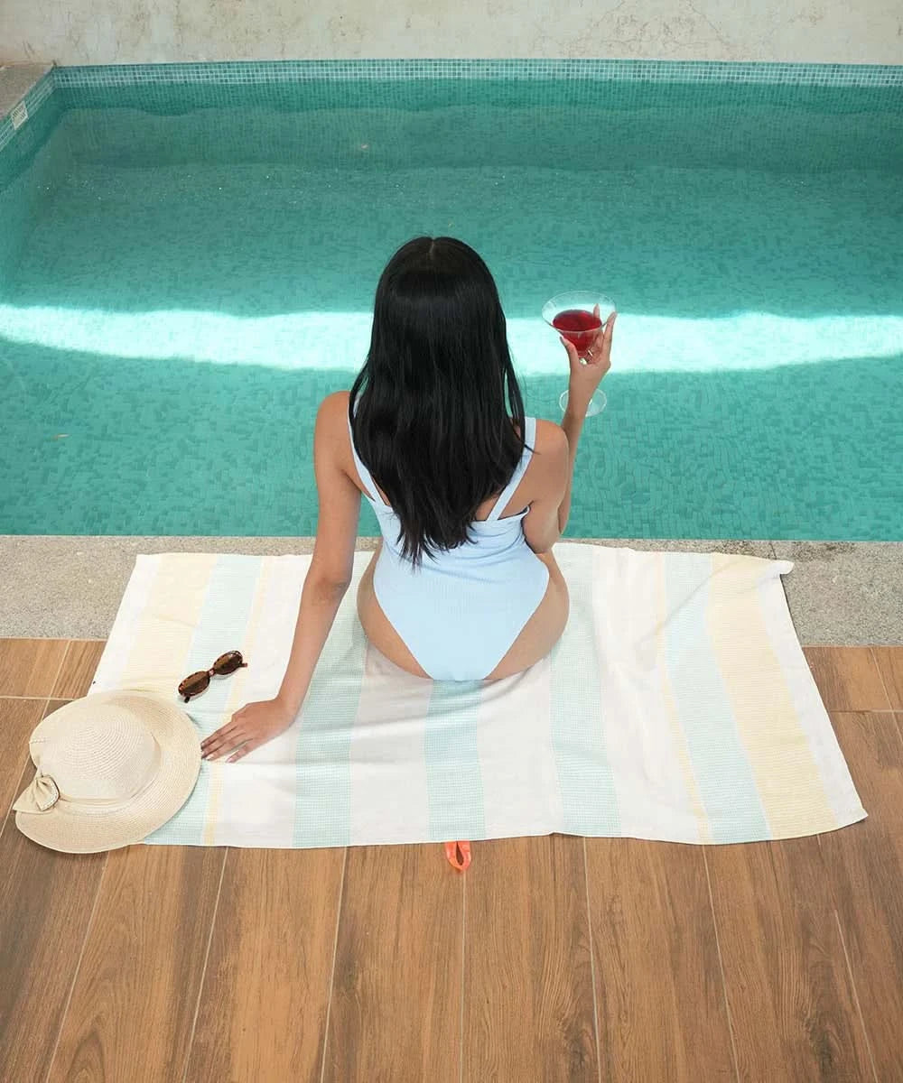 Woman sitting by a pool holding a drink on a bamboo dobby towel