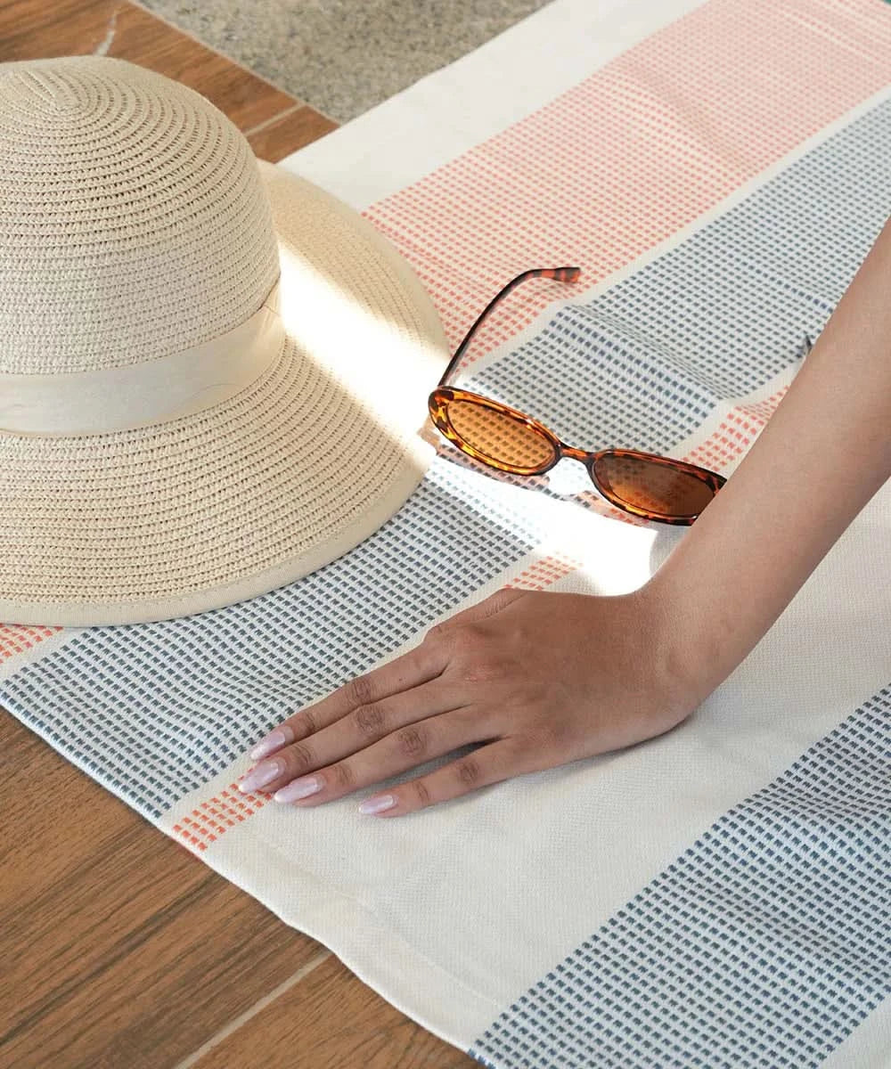Beige straw hat and sunglasses on a bamboo dobby towel with a hand reaching out