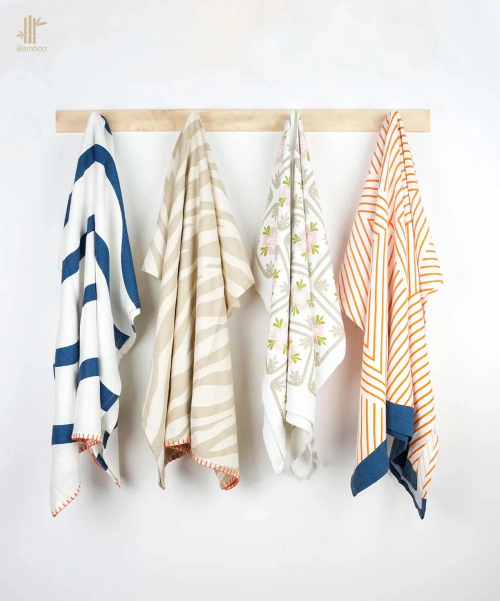 Four patterned towels hanging on a wooden rod against a white wall.