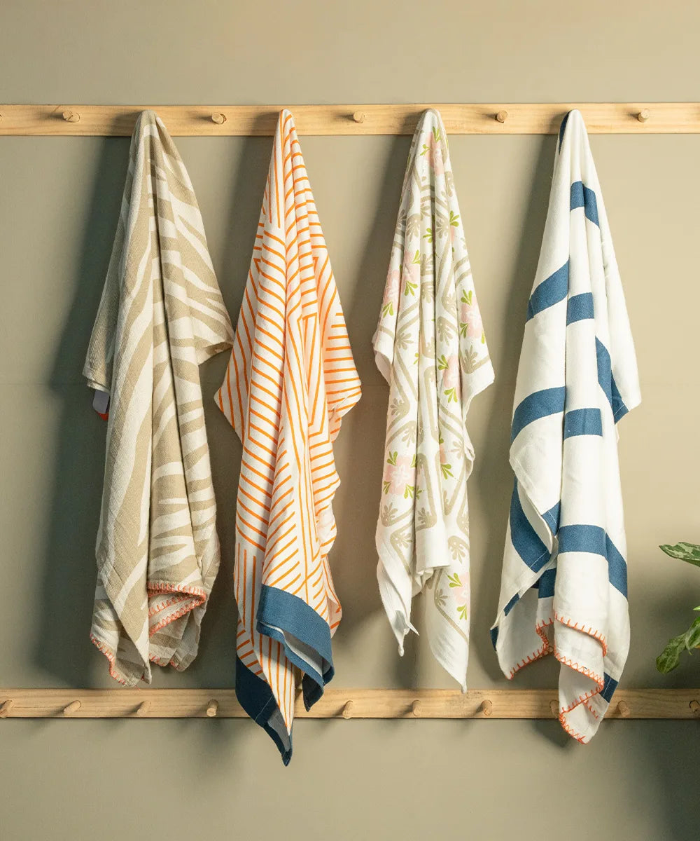 Four assorted patterned towels hanging on a wooden rack against a beige wall.