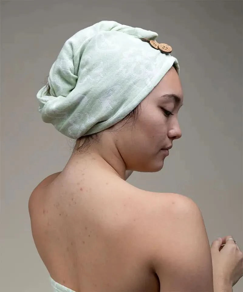 Woman with a pastel green towel wrapped around her head against a neutral background