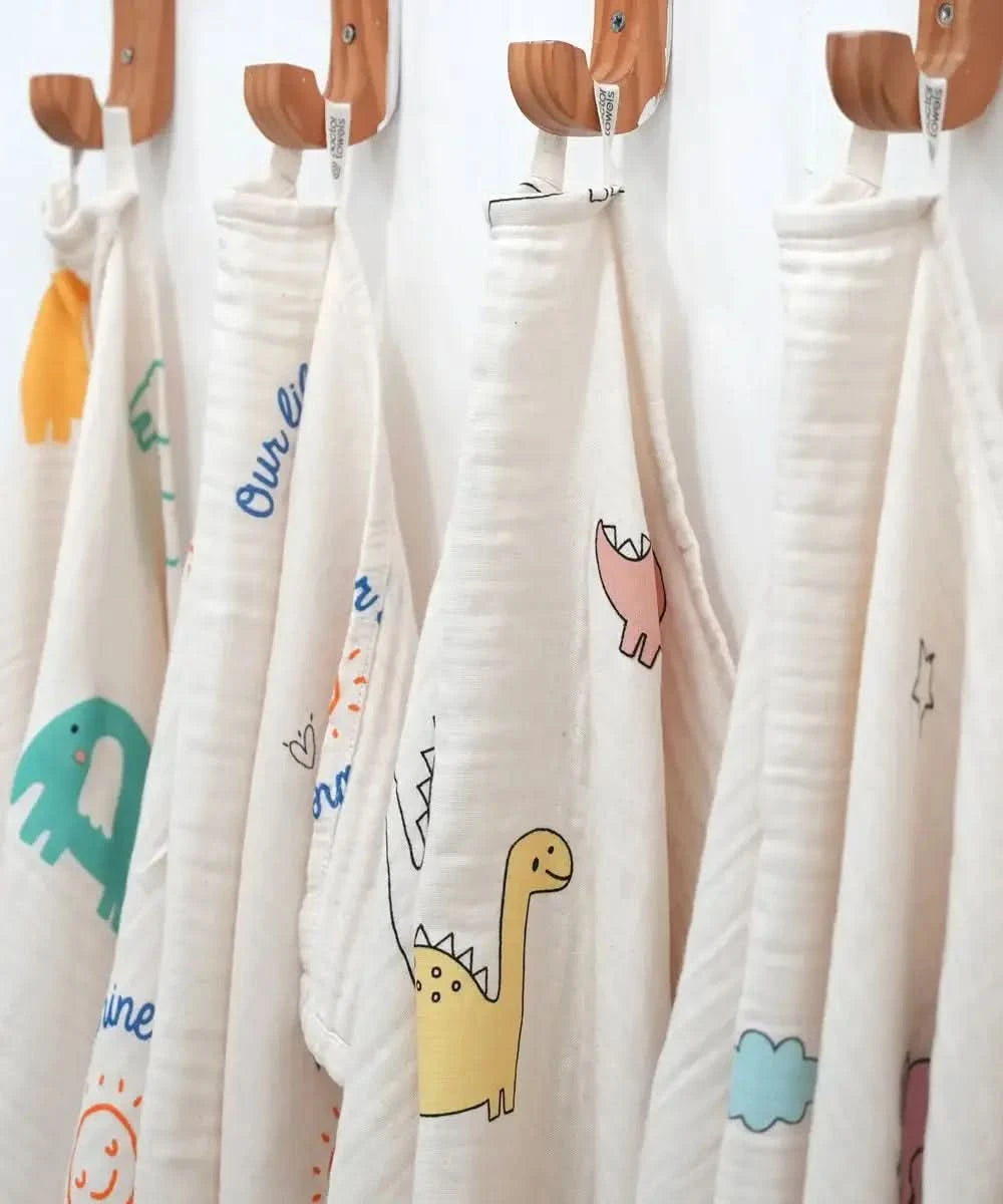 Set of bamboo baby swaddle with colorful cartoon designs hanging on wooden hooks.