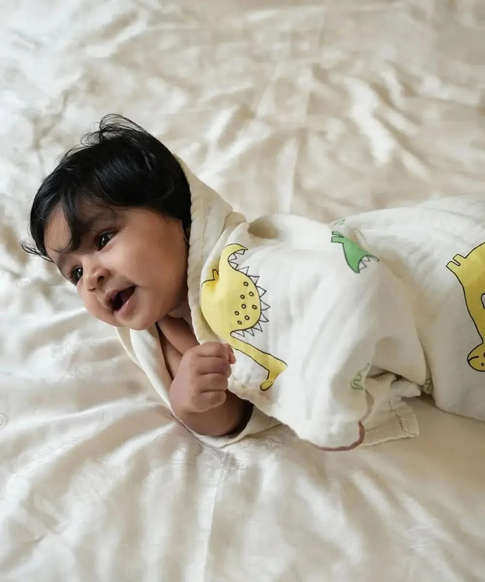 Baby wrapped in a bamboo swaddle with dinosaur patterns on a light-colored surface